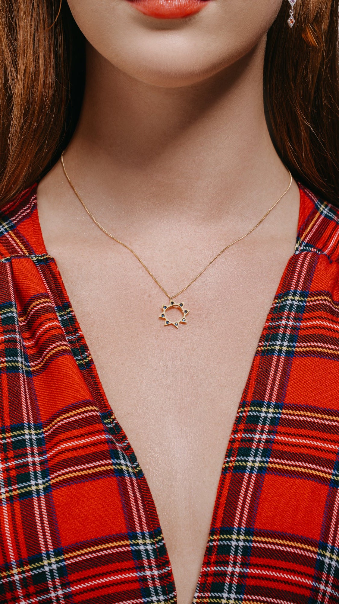 Person wearing a red plaid shirt with a gold necklace featuring a circular pendant.