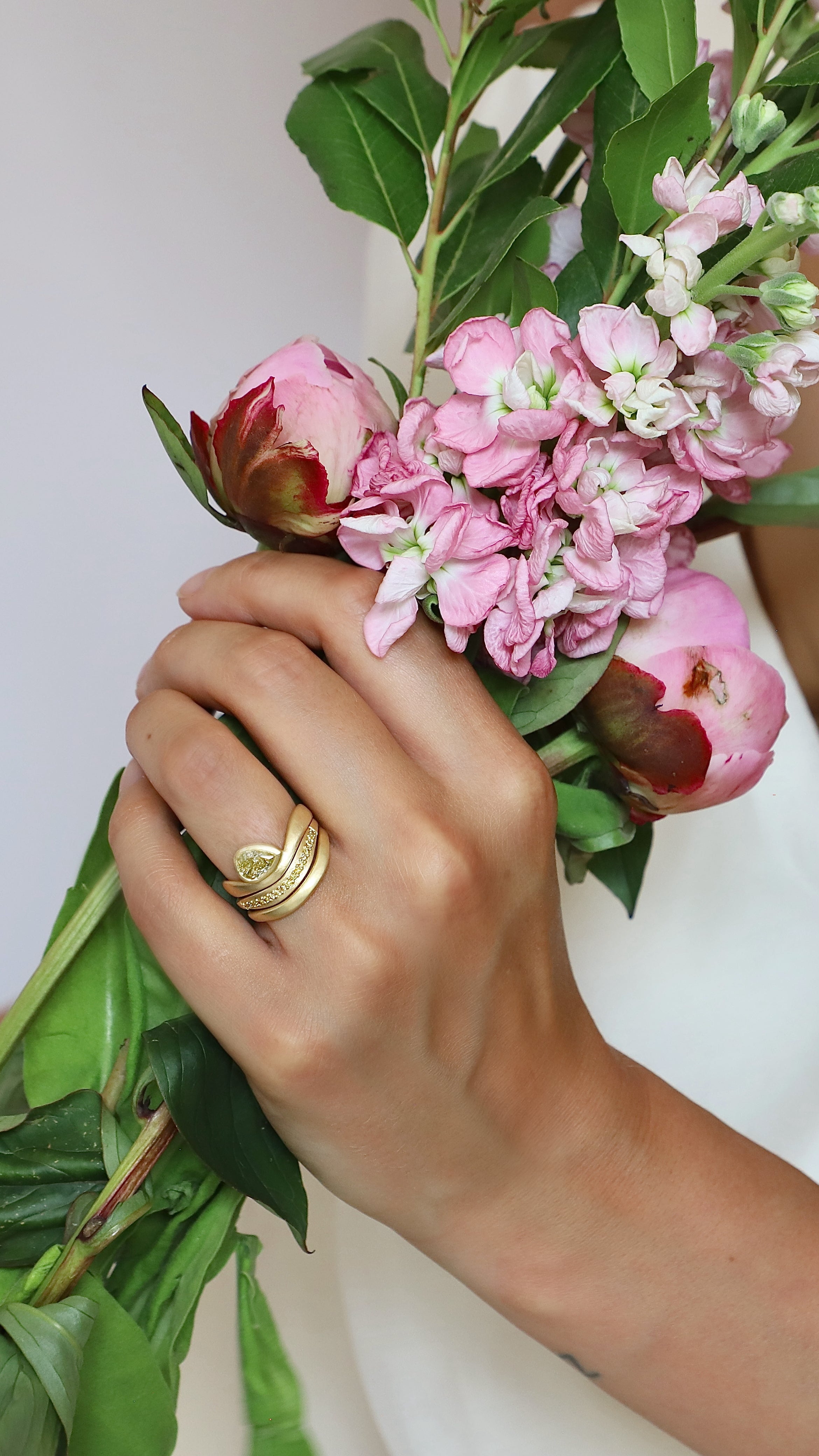 Person holding a bouquet of pink flowers with green leaves against a white background